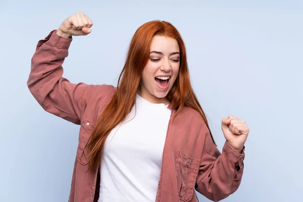 Ruiva Adolescente Sobre Isolado Fundo Azul Celebrando Uma Vitória — Fotografia de Stock