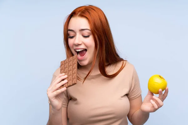 Redhead Teenager Girl Isolated Blue Background Taking Chocolate Tablet One — Stock Photo, Image