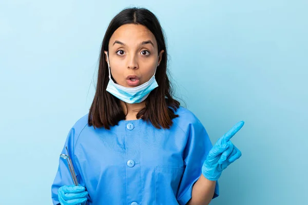 年轻的黑发混血女牙医拿着工具在与世隔绝的背景下试图在举起一个手指头的同时实现解决方案 — 图库照片