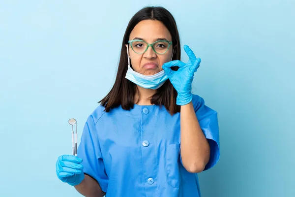 年轻的黑发混血女牙医拿着工具在与世隔绝的背景上表现出沉默的姿态 — 图库照片