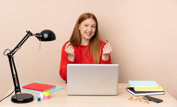 Young student woman in a workplace with a laptop making money gesture