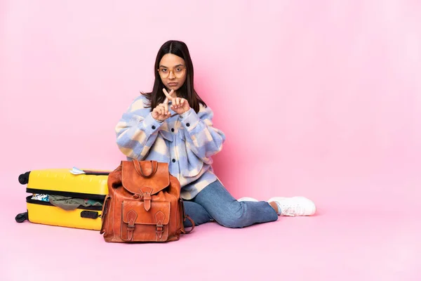 Traveler woman with a suitcase sitting on the floor making stop gesture with her hand to stop an act