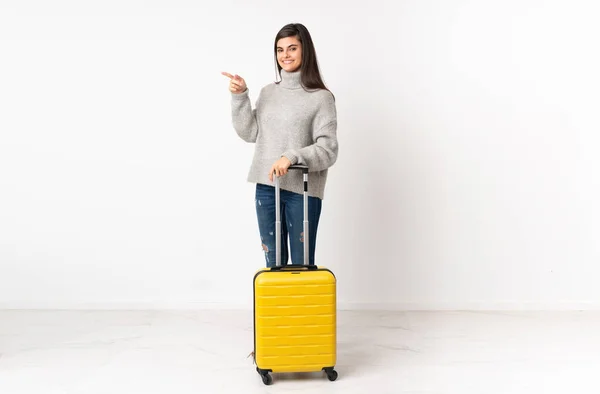 一整身的女旅行家 提着一个手提箱 越过孤立的白墙 手指指向旁边 — 图库照片