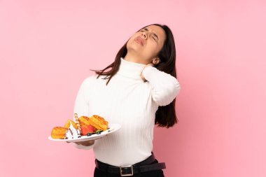 Koyu pembe arka planda kolyesi olan, gözleme tutan esmer bir kadın.