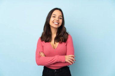 Mavi arka planda izole genç melez kadın kollarını ön cephede çapraz tutuyor.