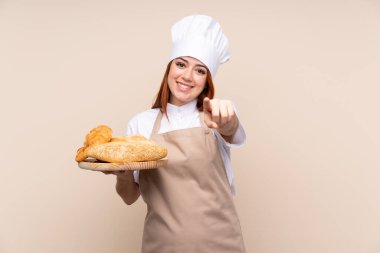 Şef üniformalı kızıl saçlı genç kız. Kadın fırıncı, elinde birkaç ekmek olan bir masayı tutarken kendine güvenen bir ifadeyle parmaklarını sana doğrultuyor.