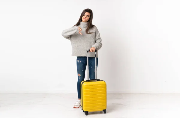 一个带着手提箱的女旅行家的完整的身体 她的手提箱穿过孤立的白墙 上面显示着拇指向下的标志 — 图库照片