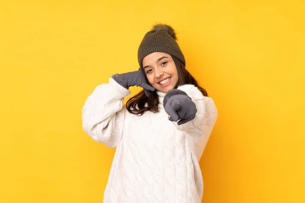 年轻女子 头戴冬帽 黄底孤零零的 做电话手势 指着前方 — 图库照片