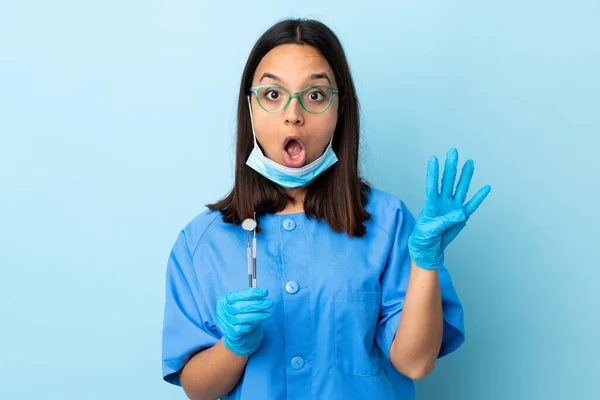 年轻的黑发男女混血的牙医女人快乐地拿着工具在与世隔绝的背景上 用手指数着四个 — 图库照片