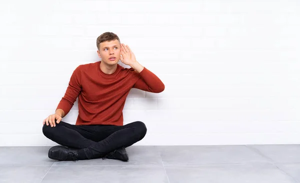 Mladý Pohledný Muž Který Sedí Podlaze Poslouchá Něco — Stock fotografie