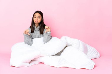 Genç melez kadın pijamasını giymiş yerde oturmuş iki eliyle baş parmağını gösteriyor.