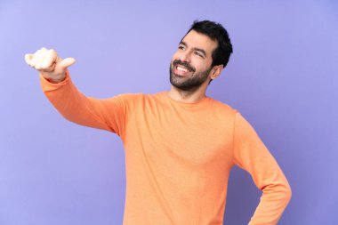 Mor arka planda beyaz tenli yakışıklı bir adam baş parmak hareketi yapıyor.