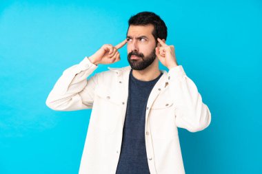 İzole edilmiş mavi arka planda beyaz kadife ceketli genç ve yakışıklı bir adamın şüpheleri ve düşünceleri var.