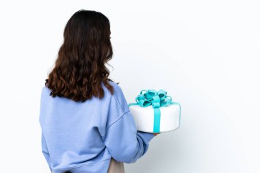 Pasta şefi, arka planda izole edilmiş beyaz arka planda büyük bir pasta tutuyor ve geriye bakıyor.