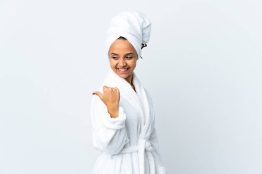 İzole edilmiş beyaz arka planda bornozlu genç bir kadın bir ürün sunmak için kenarı işaret ediyor.