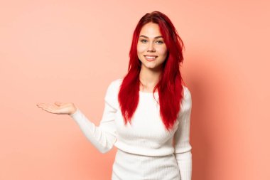 Genç kızıl saçlı kız pembe arka planda izole edilmiş bir fikir sunuyor ve gülümsüyor.