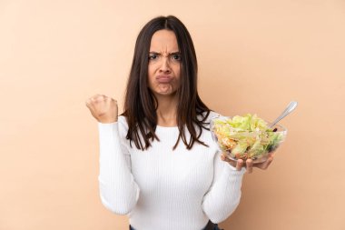 Genç esmer kız izole edilmiş arka planda salata tutuyor kızgın bir hareketle.