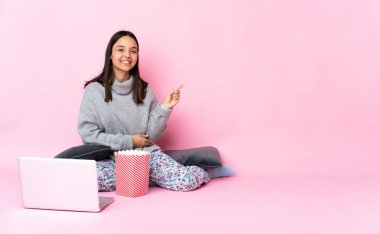 Genç melez kadın dizüstü bilgisayarda film izlerken patlamış mısır yiyor.