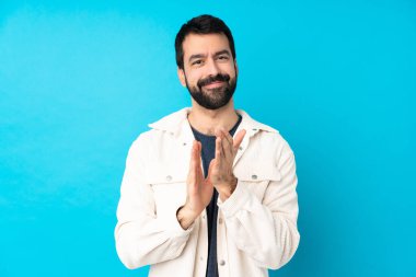 Beyaz kadife ceketli genç ve yakışıklı bir adam münferit mavi arka planda bir konferanstan sonra alkış tutuyor.