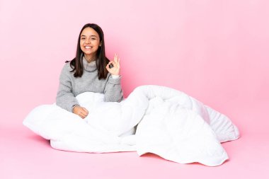 Genç melez kadın pijamasını giymiş yerde oturmuş parmaklarıyla işaret veriyor.