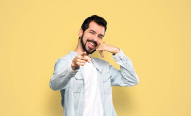 Sakallı yakışıklı bir adam telefon ediyor ve sarı arka plan üzerinde ön tarafı işaret ediyor.