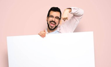 Handsome man with beard holding an empty placard over isolated pink background