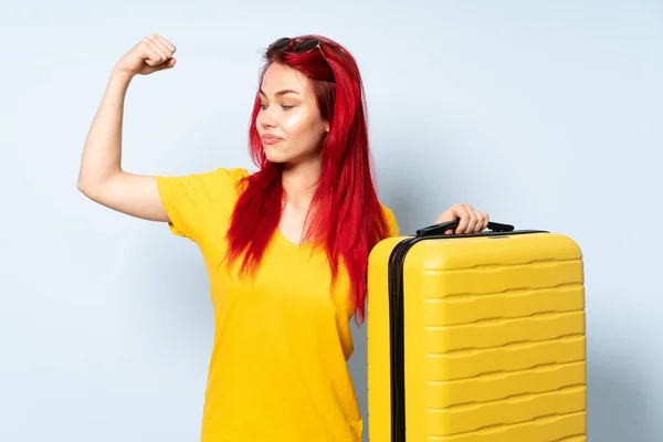 带着一个蓝色背景的手提箱的旅行女孩做着强有力的手势 — 图库照片