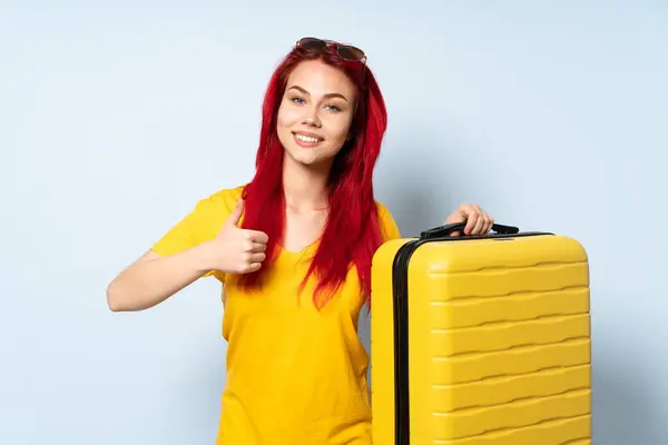带着一个蓝色背景的手提箱的旅行女孩举起一个大拇指 — 图库照片