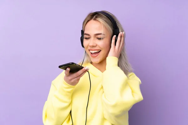 자주색 배경의 소녀가 핸드폰으로 음악을 노래를 부르는 — 스톡 사진