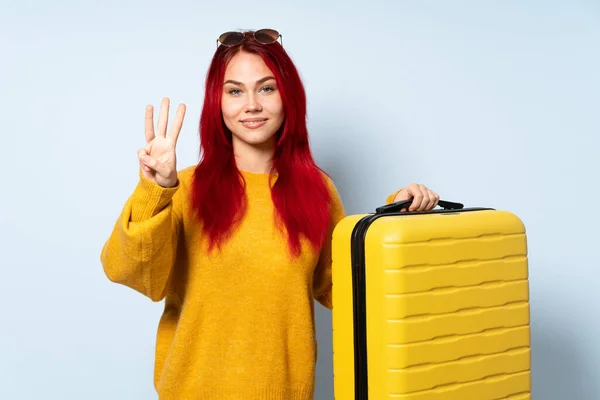 旅行的女孩拿着一个蓝色背景的手提箱 高兴极了 用手指数着三个 — 图库照片