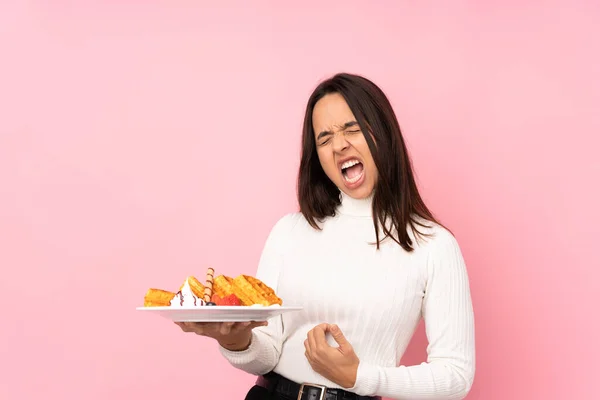 Joven Morena Sosteniendo Gofres Sobre Fondo Rosa Aislado Haciendo Gesto —  Fotos de Stock