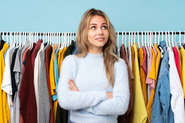Teenager Russian girl buying some clothes isolated on blue background looking up while smiling