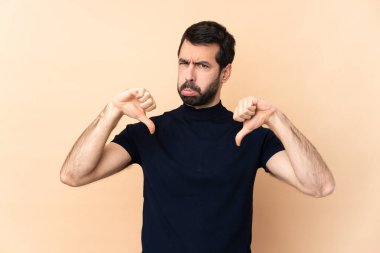 Kafkasyalı yakışıklı adam izole edilmiş arka planda baş parmağını aşağı gösteriyor.