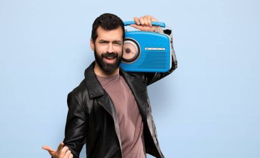 Handsome man with beard holding a radio over isolated blue background