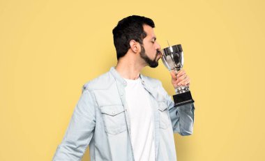 Handsome man with beard holding a trophy over isolated yellow background