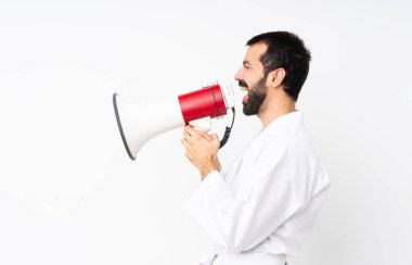 Young man doing karate over isolated white background shouting through a megaphone