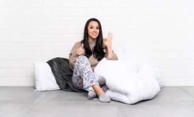 İçerde pijamalı genç Kolombiyalı kız. Tamam işareti gösteriyor ve el hareketi yapıyor.