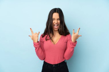 Genç melez kadın mavi arka planda izole edilmiş kaya jestleri yapıyor.
