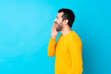 İzole edilmiş mavi arka planda genç beyaz adam ağzı sonuna kadar açık bağırıyor.