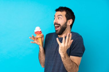 Kornet dondurması olan genç bir adam izole edilmiş mavi bir arka plan ve şaşırtıcı bir yüz ifadesi var.