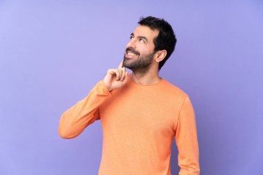 Kafkasyalı yakışıklı bir adam mor arka plandan izole edilmiş bir şekilde yukarı bakarken bir fikir düşünüyor.