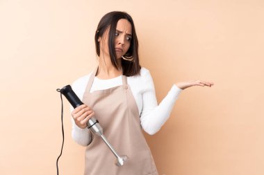 El blenderi kullanan genç esmer kız izole edilmiş arkaplanda kopyalama alanı tutuyor.