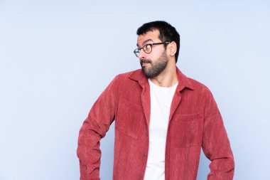 Mavi arka planda kadife ceket giyen genç beyaz adam şüpheli hareketler yapıyor.