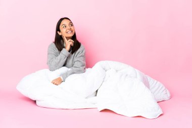 Genç melez kadın pijama giyip yerde oturuyor. Kafasını kaldırıp bakarken bir fikir düşünüyor.