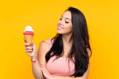 Kornet dondurması tutan genç Kolombiyalı kız izole edilmiş sarı arka planda mutlu bir ifadeyle.