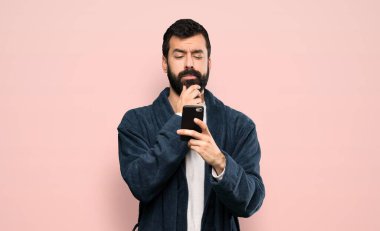 Pijamalı sakallı bir adam düşünüyor ve pembe arka plan üzerinden mesaj gönderiyor.