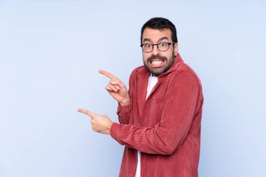 Mavi arka planda kadife ceket giyen genç beyaz adam korkmuş ve yan tarafı işaret ediyor.