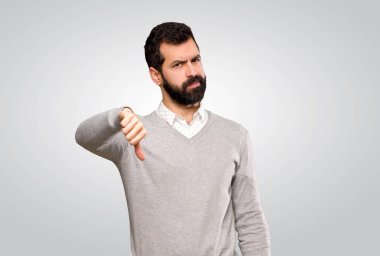 Yakışıklı adam, izole edilmiş gri arkaplanda olumsuz ifade ile baş parmağını aşağı gösteriyor.