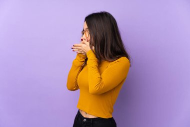 Mor arka planda izole edilmiş genç bir ırk kadını ağzını kapatıyor ve yan tarafa bakıyor.