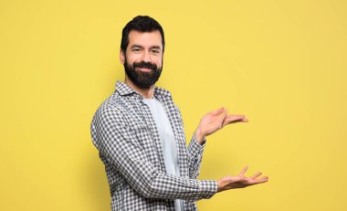 Yakışıklı ve sakallı bir adam. Davet edildiği için ellerini yana uzatıyor.